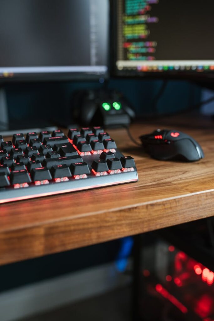 Contemporary personal computer monitors with programming codes placed on desk with backlit keyboard and mouse in light room